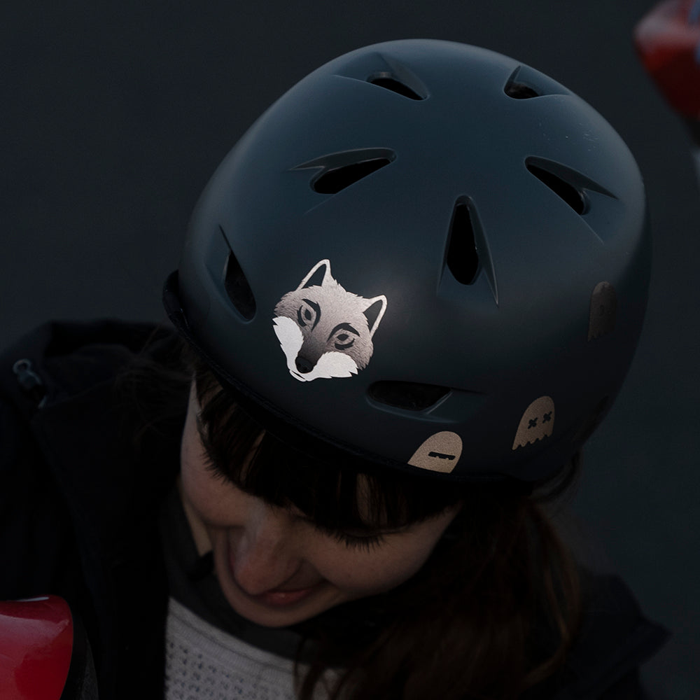Frau mit grauem Helm und reflektierendem Wolf Aufkleber vorne, sieht nach unten,