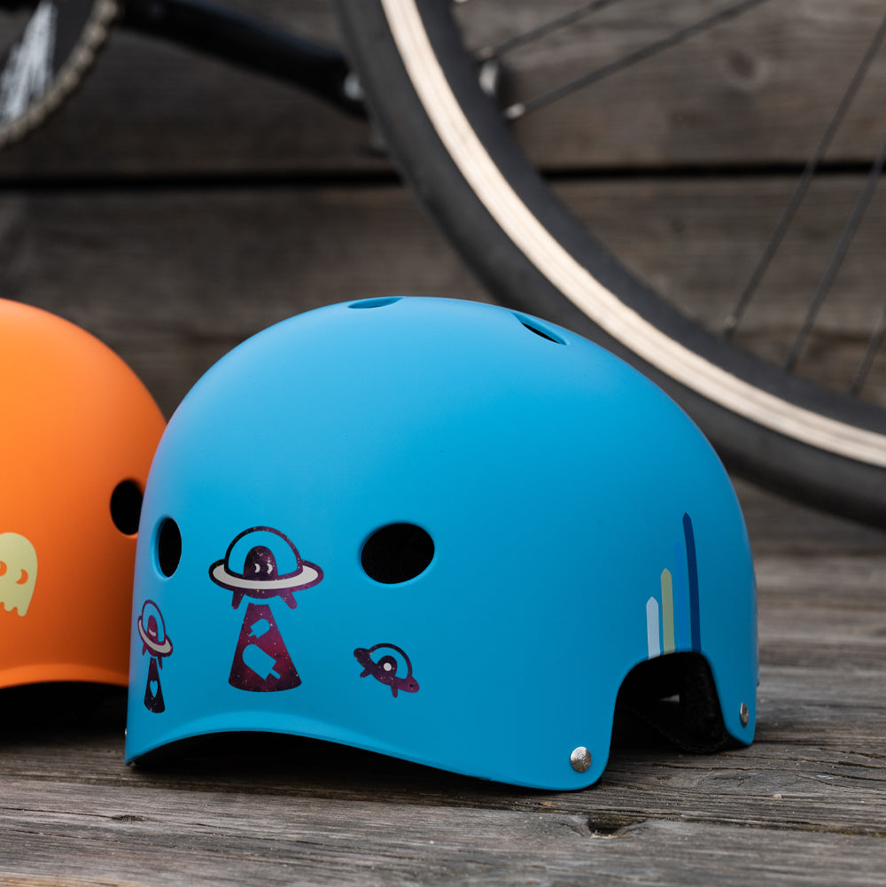 Blauer Fahrradhelm auf dem Boden vor einem Fahrrad, mit UFO Stickern hinten