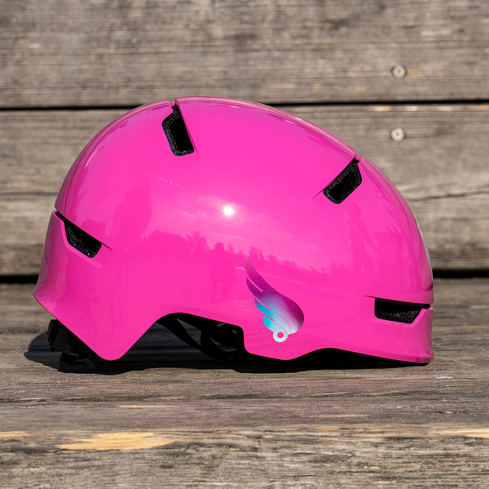 Pinker Fahrradhelm liegt auf Holz, Seitenansicht mit reflektierendem Flügel Aufkleber